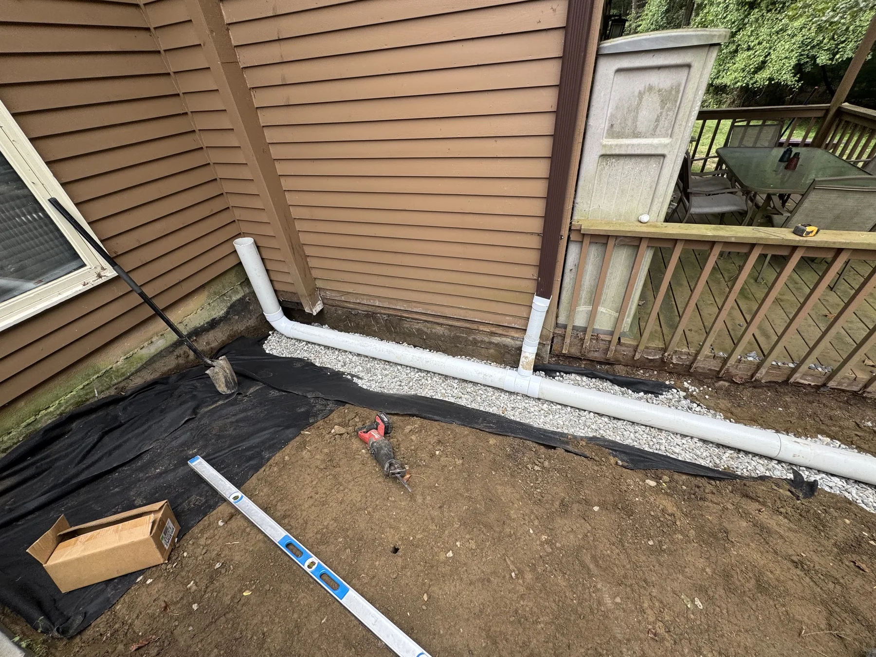 Drainage pipe installation with stone bedding beside a property